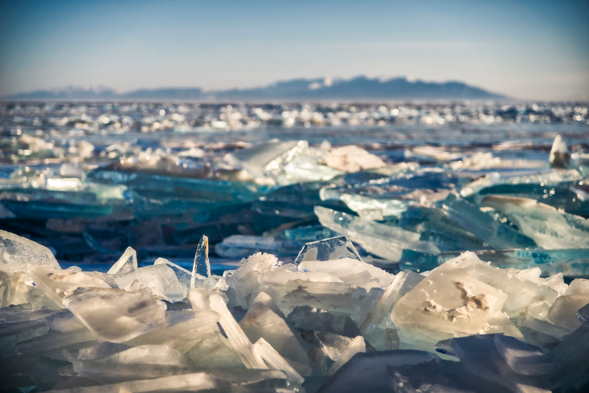 Нагромождение бирюзовых и белых льдин до горизонта, вдали горы в дымке, Байкал